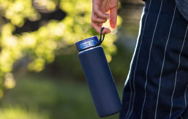A blue reusable water bottle hanging from the hand of someone walking in a park
