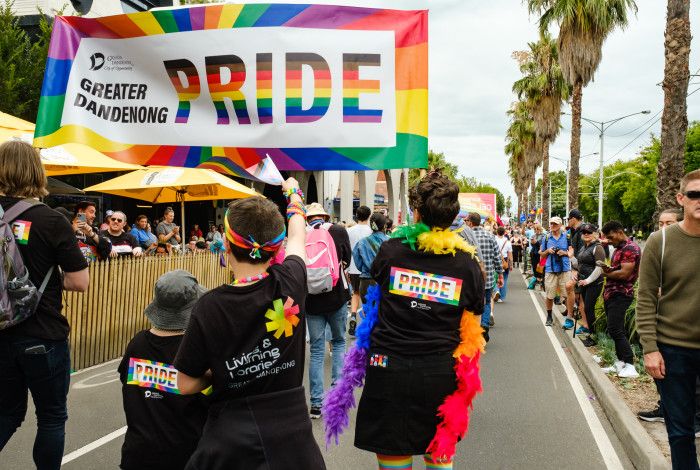 A group of people walking down a street lined by crowds under a banner that reads Greater Dandenong Pride