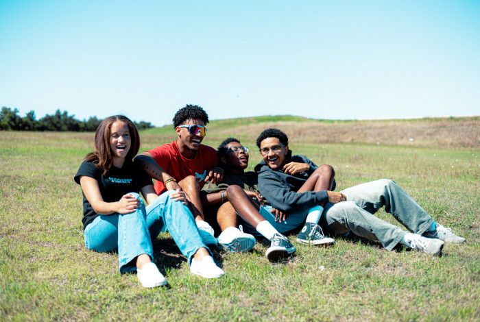 Four young people sitting together and laughing on a grassy hill.
