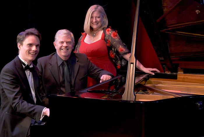 Three people sitting at a piano