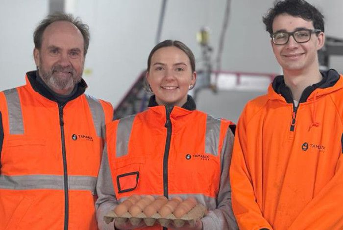 Three people smiling and holding a carton of eggs