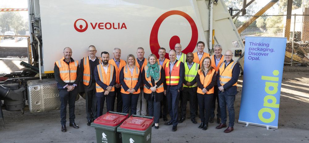 A group of people in high vis vests stood in front of a garbage truck.