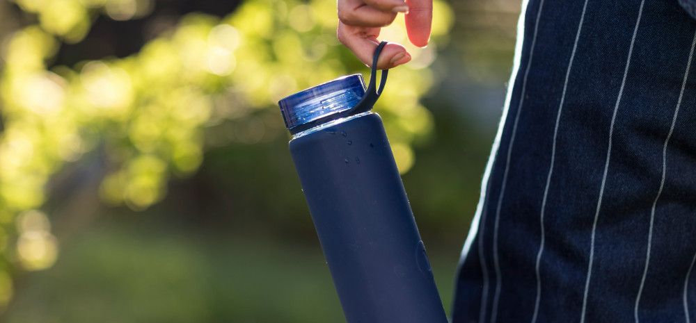 A blue reusable water bottle hanging from the hand of someone walking in a park