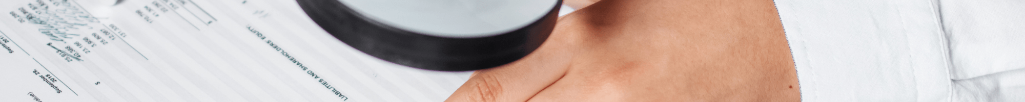 A business person using a magnifying glass and calculator to audit documents.