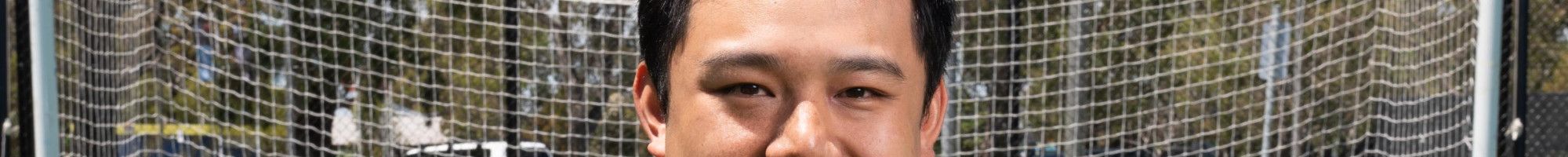 A man in a dark suit crouches on one knee on a synthetic soccer pitch while holding an orange soccer ball.
