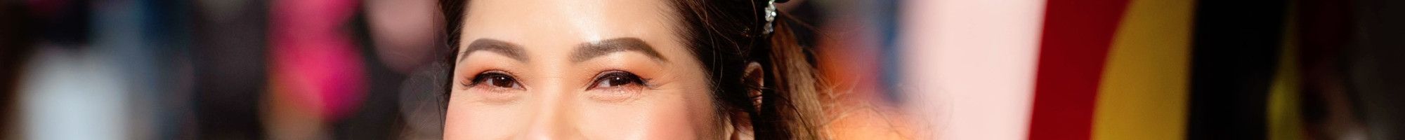 A smiling woman in a black jacket stands side on and smiles to the camera with an Aboriginal flag in the background.