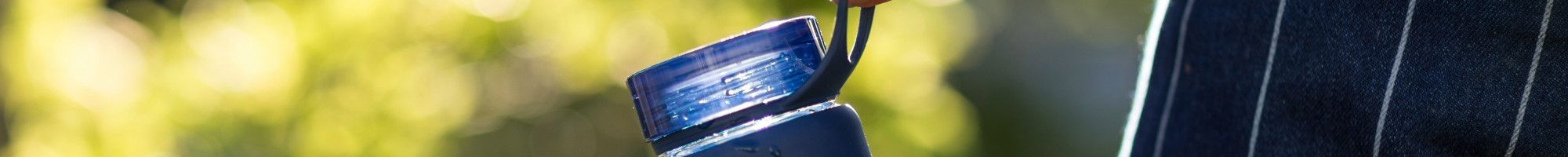 A blue reusable water bottle hanging from the hand of someone walking in a park