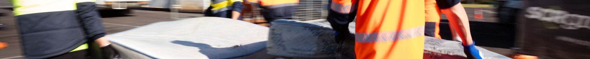 People in hi-vis carrying a mattress